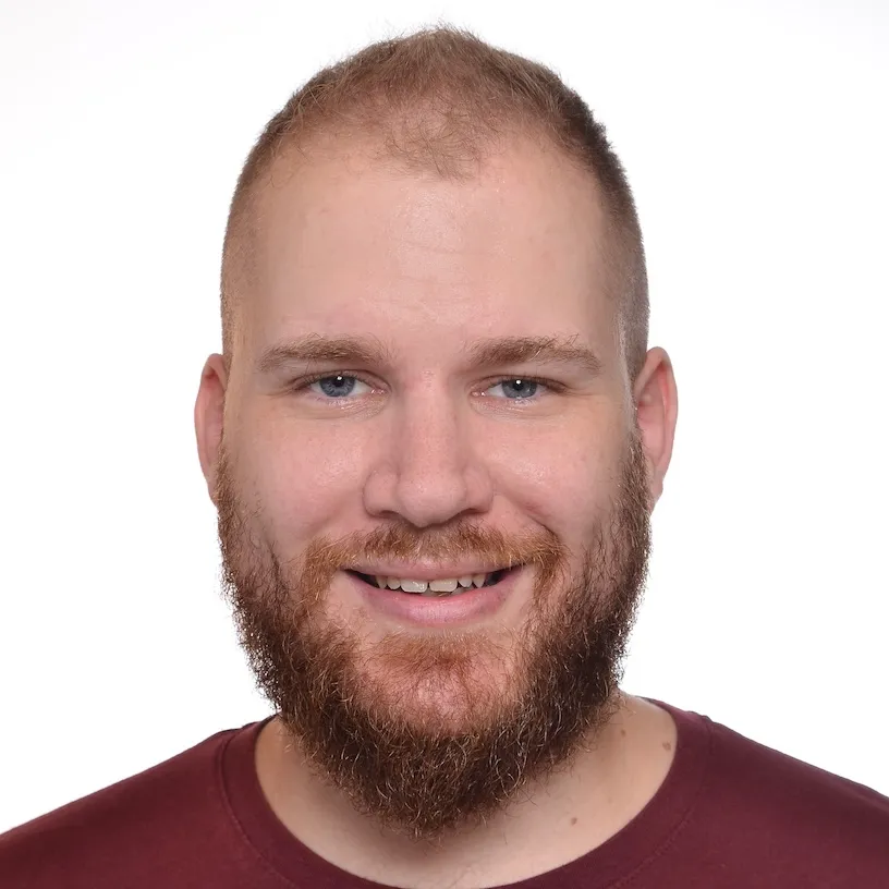 A portrait of a man in his thirties with blond hair and blue eyes, wearing a red shirt and smiling at the camera